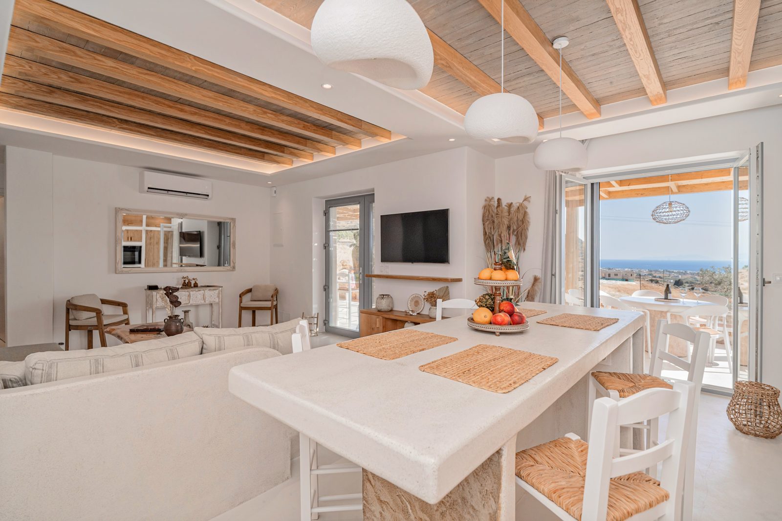 Open-plan living and kitchen area of Villa A in Naxos with timber ceiling beams and sea view doors
